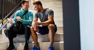 Two friends sitting on a flight of stairs after a workout laughing together