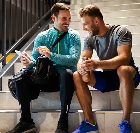 Two friends sitting on a flight of stairs after a workout laughing together