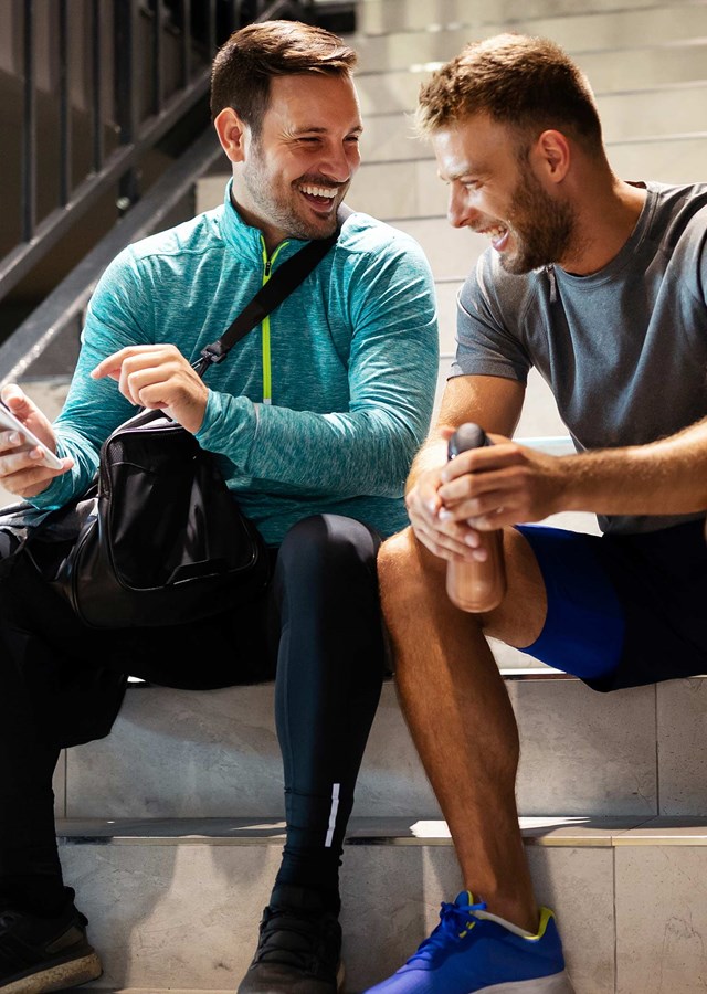 Two friends sitting on a flight of stairs after a workout laughing together