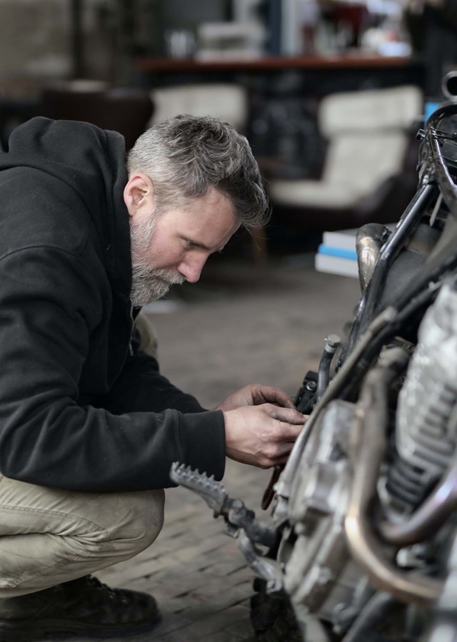 A mechanic working on a motorbike in a garage.