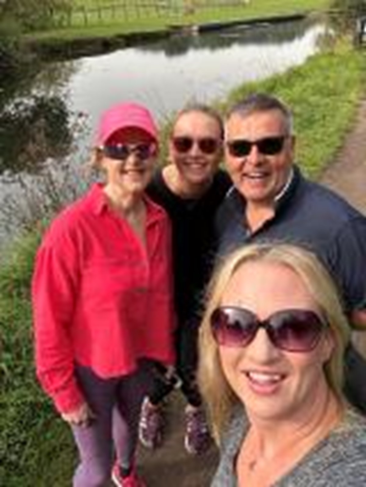 Four smiling friends in sunglasses take a selfie together on a canal towpath.