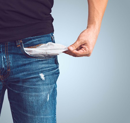 A person standing pulling their pocket out of their jeans to show it is empty and they are in debt