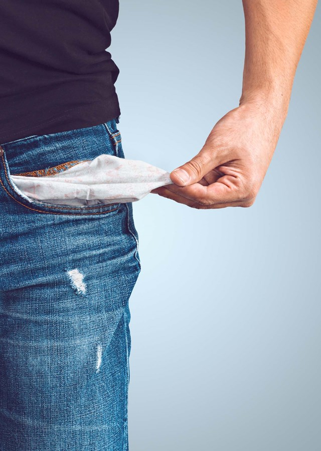 A person standing pulling their pocket out of their jeans to show it is empty and they are in debt