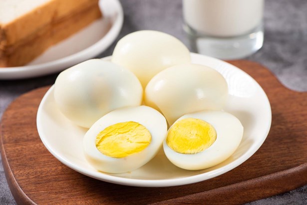Four whole hard boiled eggs in a shallow bowl. The front egg is sliced in half.