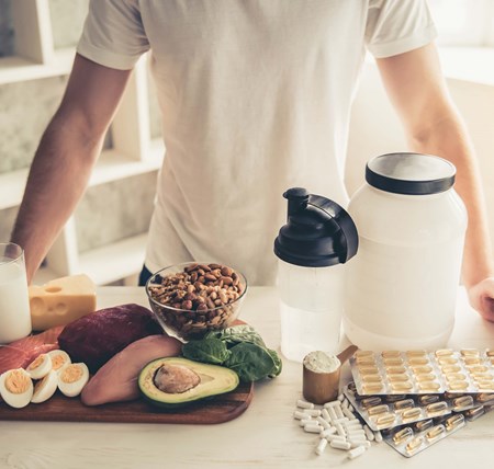 A person standing at a kitchen counter which has a variety of healthy nutritional foods on it to aid physical activity