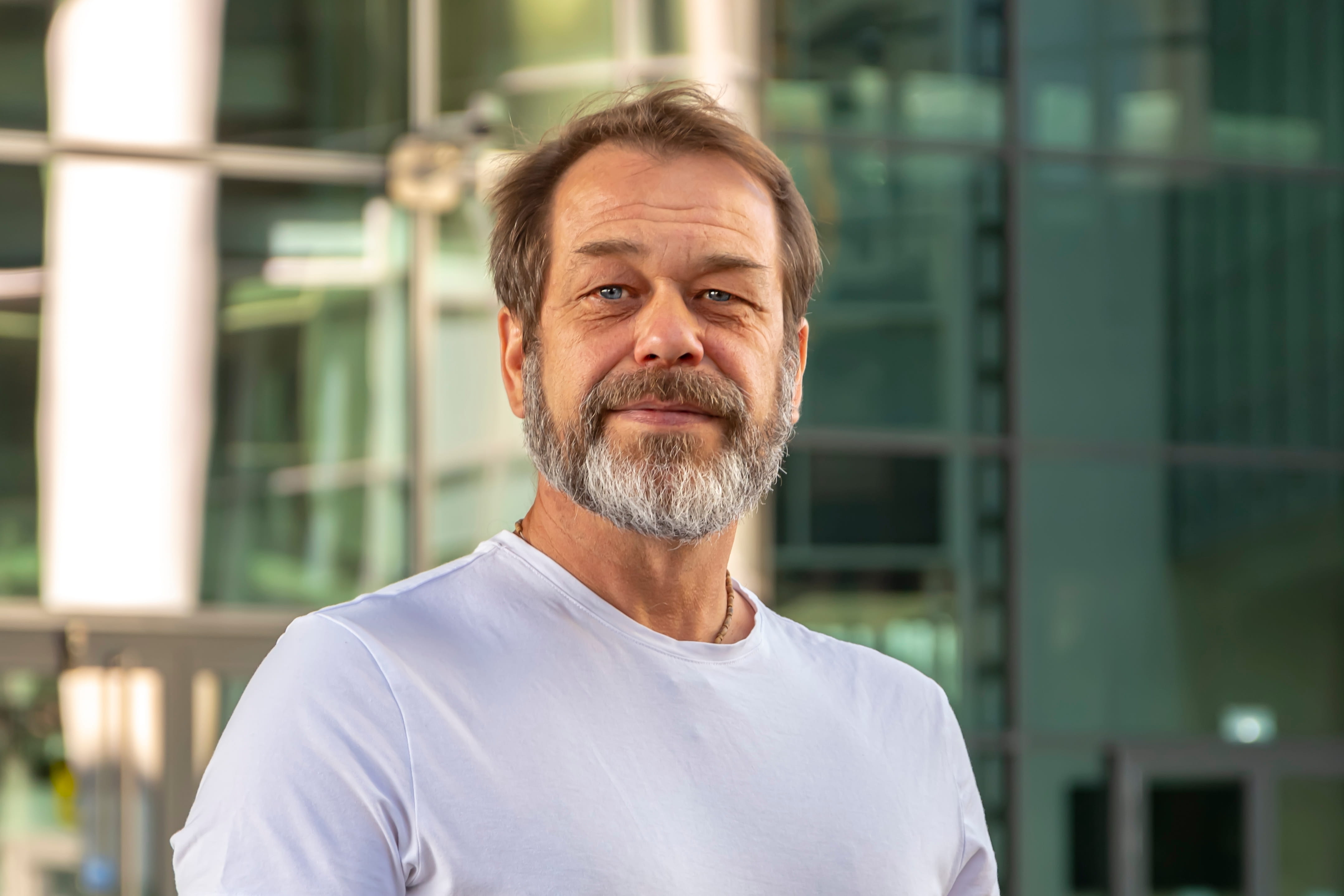 Ian's story - a man 56 years old with a beard and an athletic build against the backdrop of modern city buildings, looks at the camera.