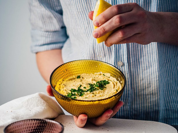 man squeezing a lemon into a bowl of hummus