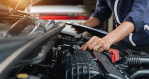 Vehicle technician (mechanic) examining a car engine in an automotive workshop (garage)