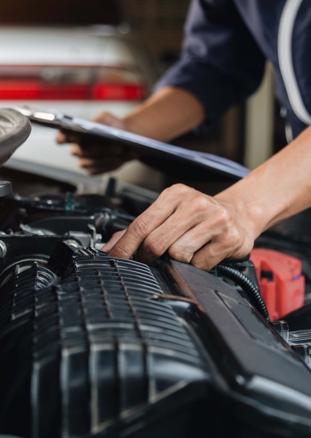 Vehicle technician (mechanic) examining a car engine in an automotive workshop (garage)