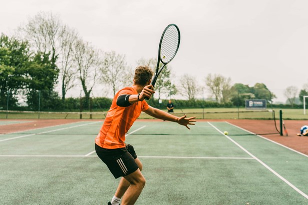 Person keeping fit by playing tennis outside on a tennis court