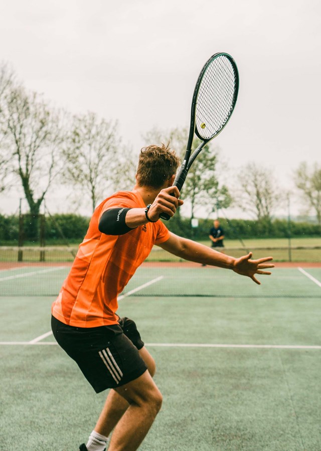 Person keeping fit by playing tennis outside on a tennis court