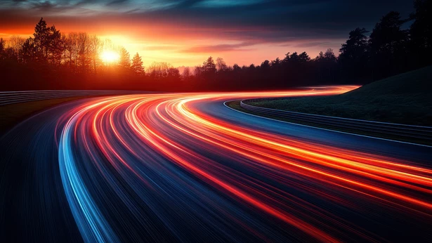 Long-exposure red and blue light trails curving along a racetrack at sunset