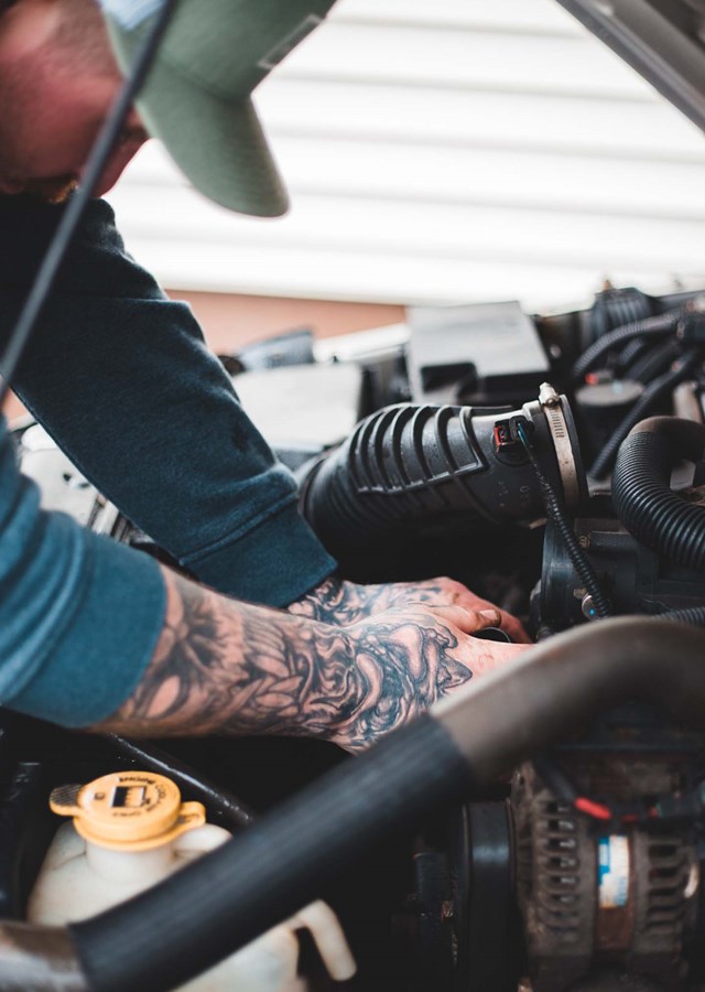 Tattooed vehicle technician fixing car engine considering changes in the industry and whether their job is at risk