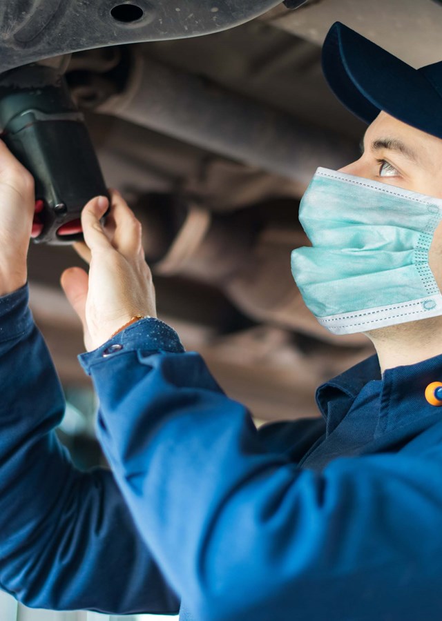 Mechanic wearing a face mask working on the underside of a car