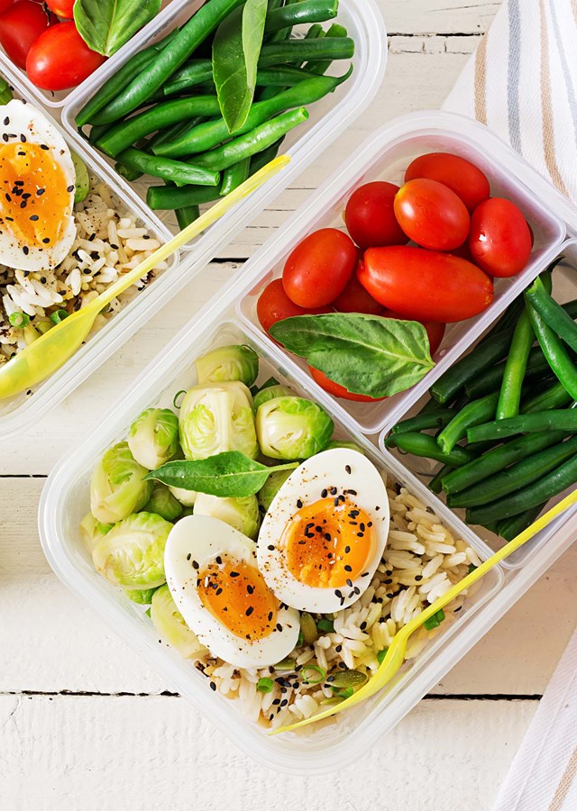 Two lunchboxes filled with colourful healthy foods ready to enjoy on the go. There is a red apple to one side of the boxes, and a green pear to the other.