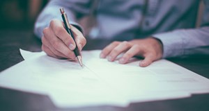Person in smart clothes amending or writing a cover letter using a pen. Making sure they include relevant information to secure a job interview