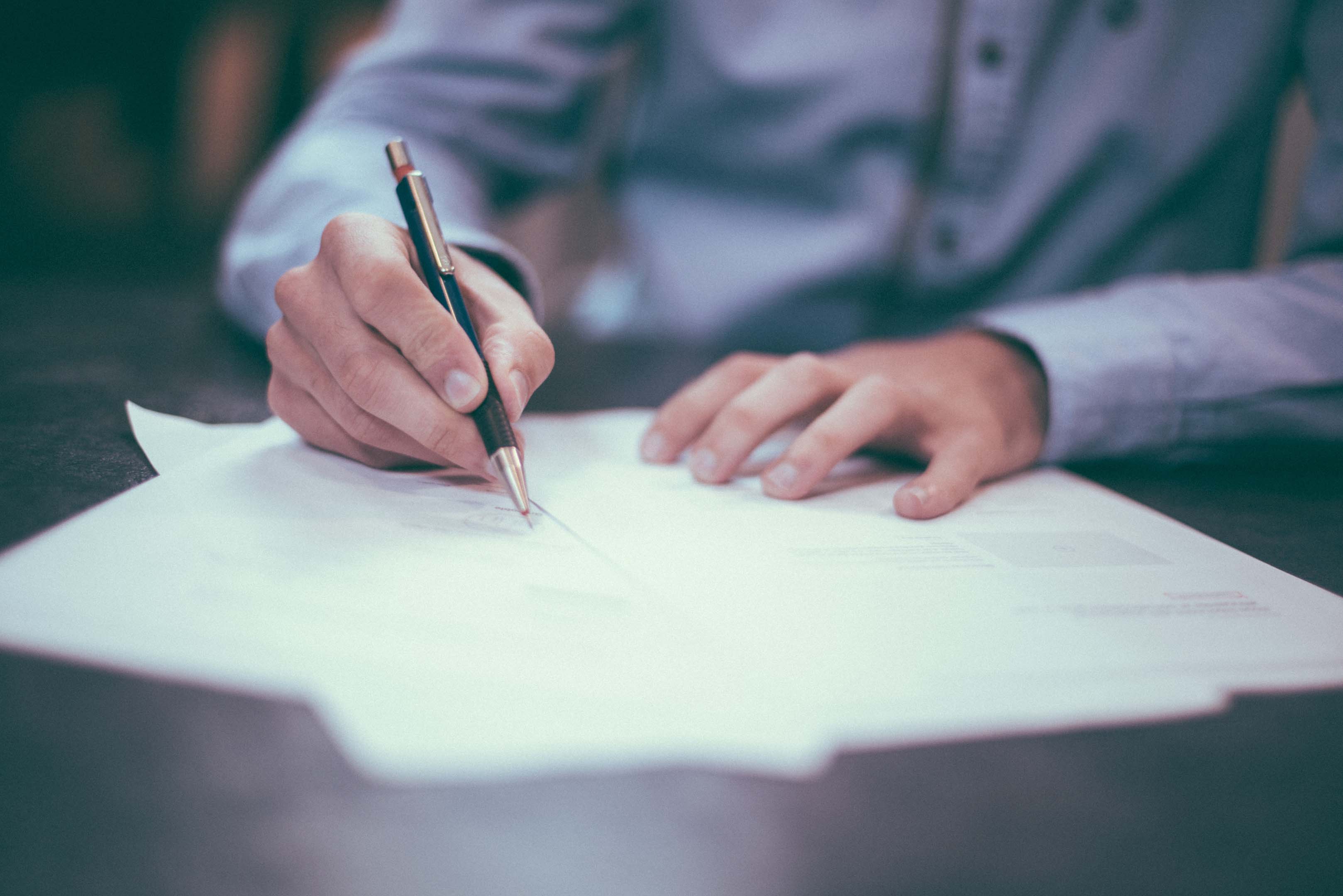 Person in smart clothes amending or writing a cover letter using a pen. Making sure they include relevant information to secure a job interview