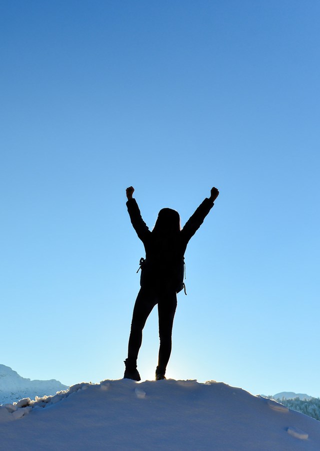 Person stood on top of a snowy mountain top celebration climbing to the summit overlooking the countryside and mountain range