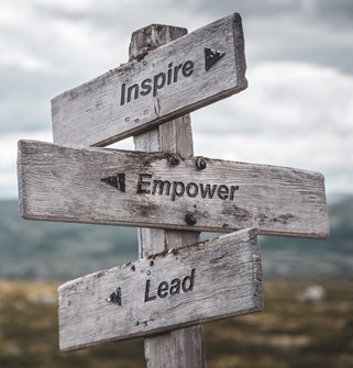 Weathered wooden signpost with three arrows reading "Inspire", "Empower" and "Lead".