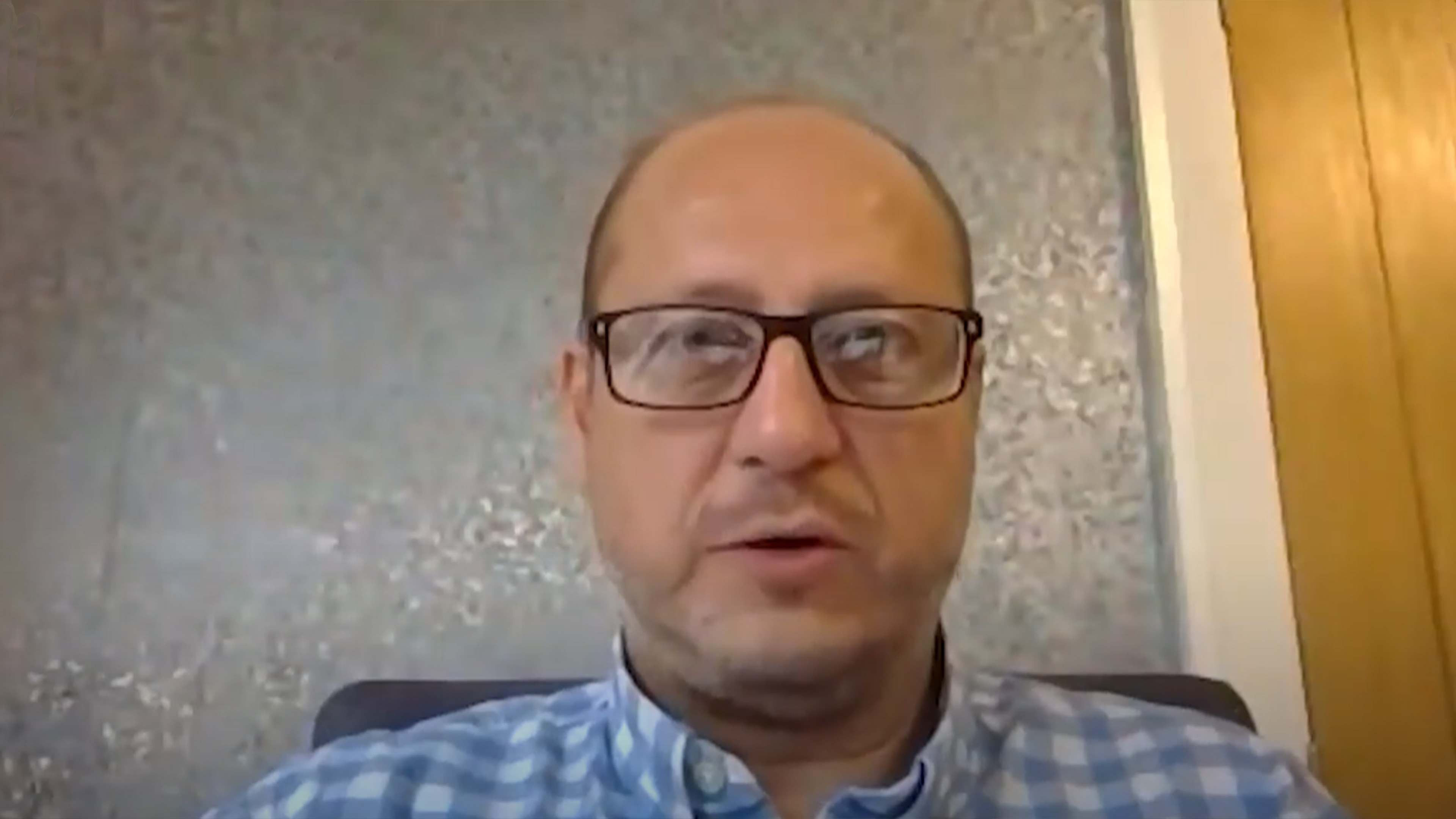 Jake, a man in glasses and a blue checked shirt, speaking to camera during a video call.