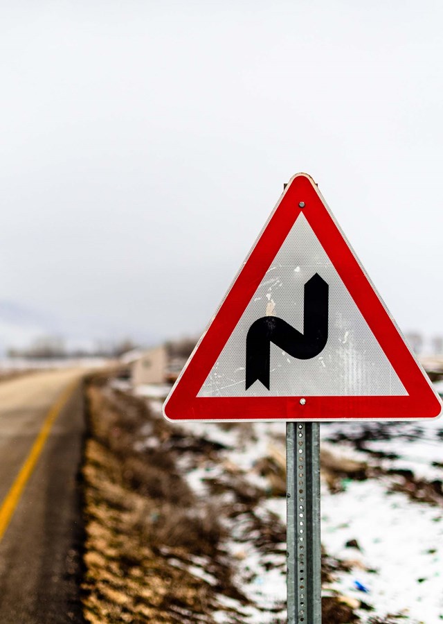 Road sign showing tight corners ahead next to a road which is surrounded in snow