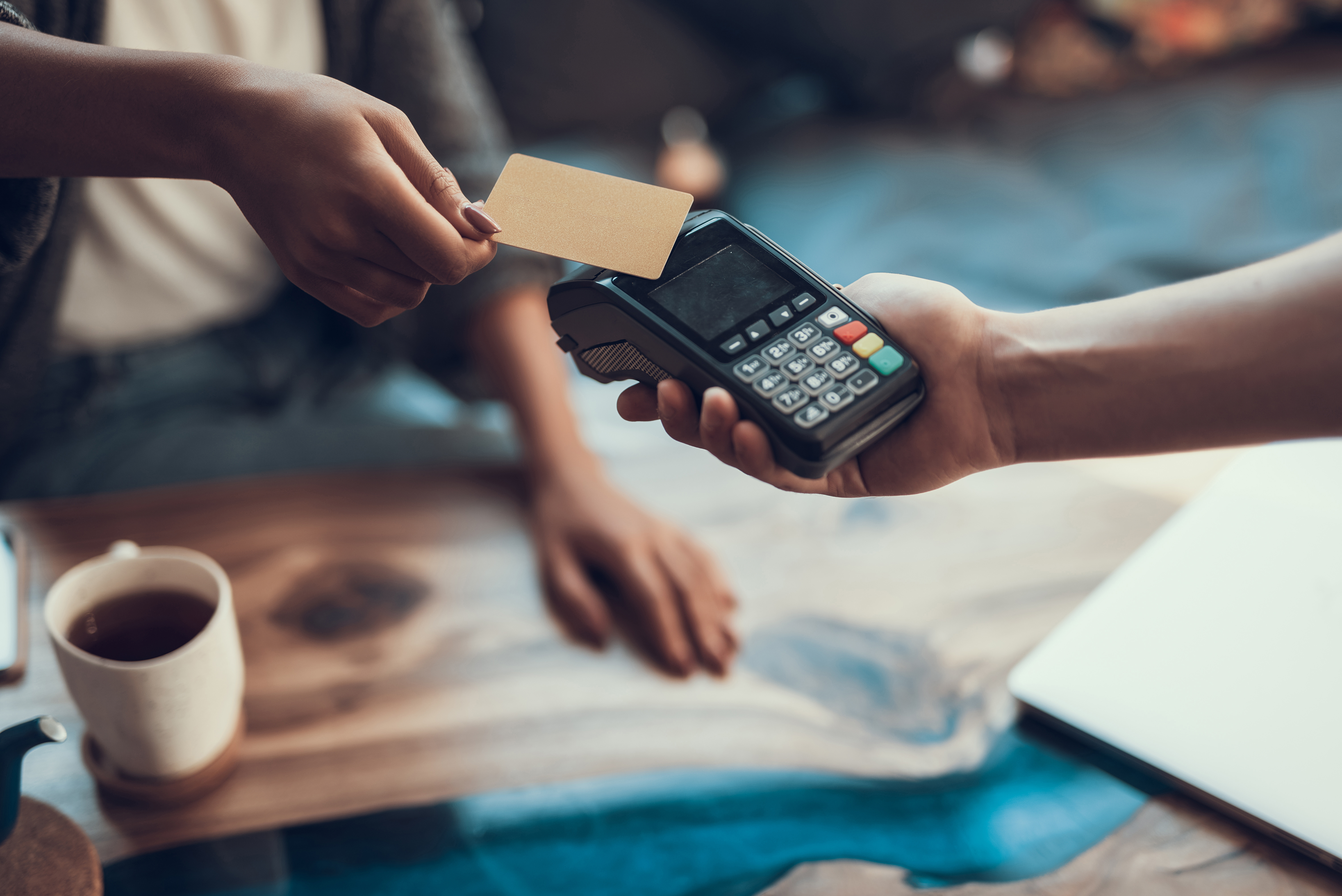A person making a contactless payment by tapping a bank card on a card machine held by another person.
