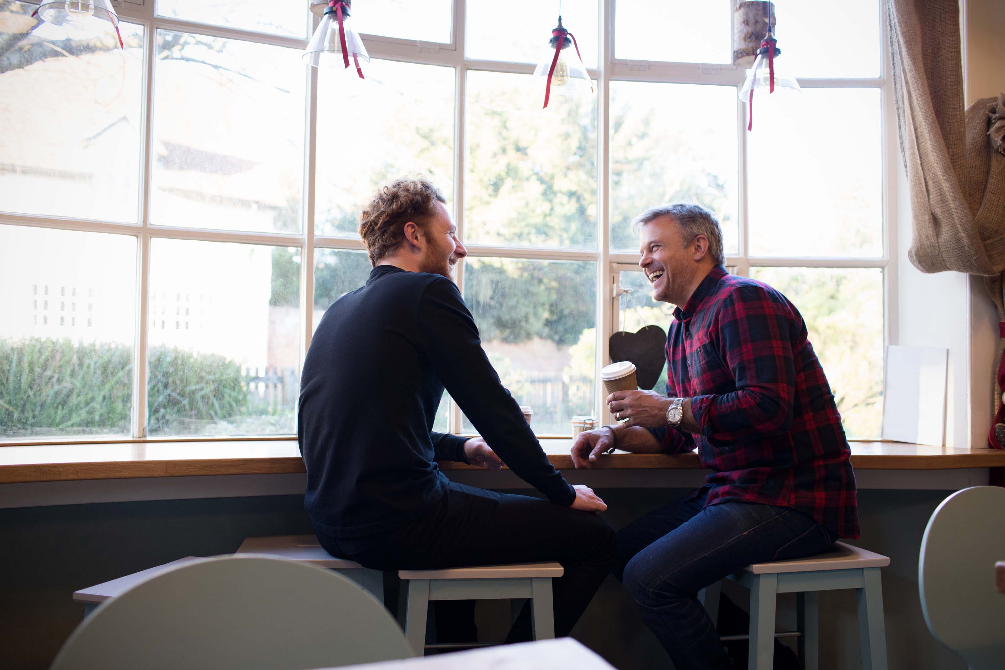 Two people sitting on stools in a cafe enjoying a coffee together and reconnecting