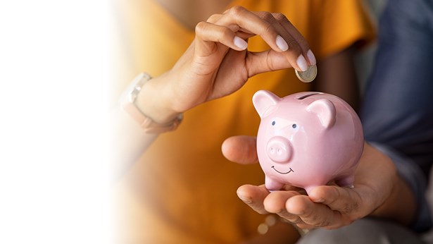 A woman dropping a coin into a pink piggy bank held in another person's hands.