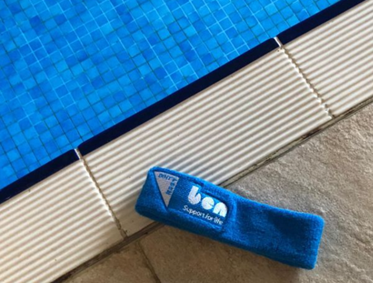 Blue Ben 'Support for life' sweatband resting on tiles at the edge of a swimming pool.