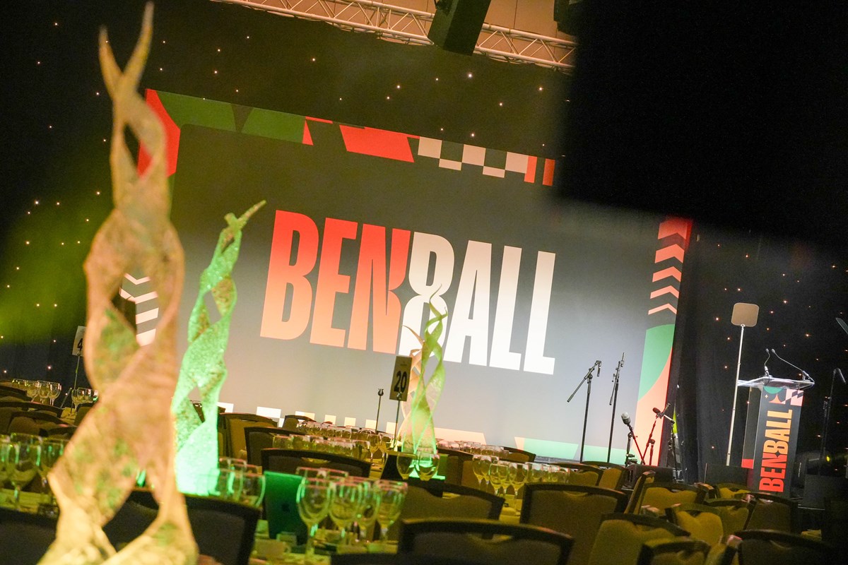 Ben Ball venue set up before guests arrive, with a large 'Ben Ball' stage screen, lit table centrepieces and rows of set tables.