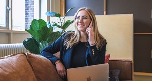 Woman in smart clothing, sitting with laptop, smiling while having a telephone interview