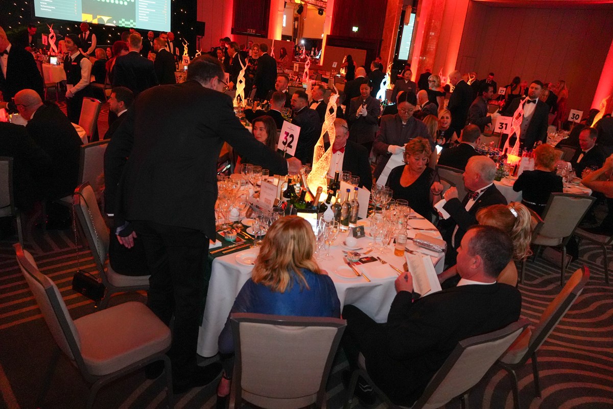 Guests in black tie seated at numbered round tables in a red-lit ballroom at the Ben Ball.