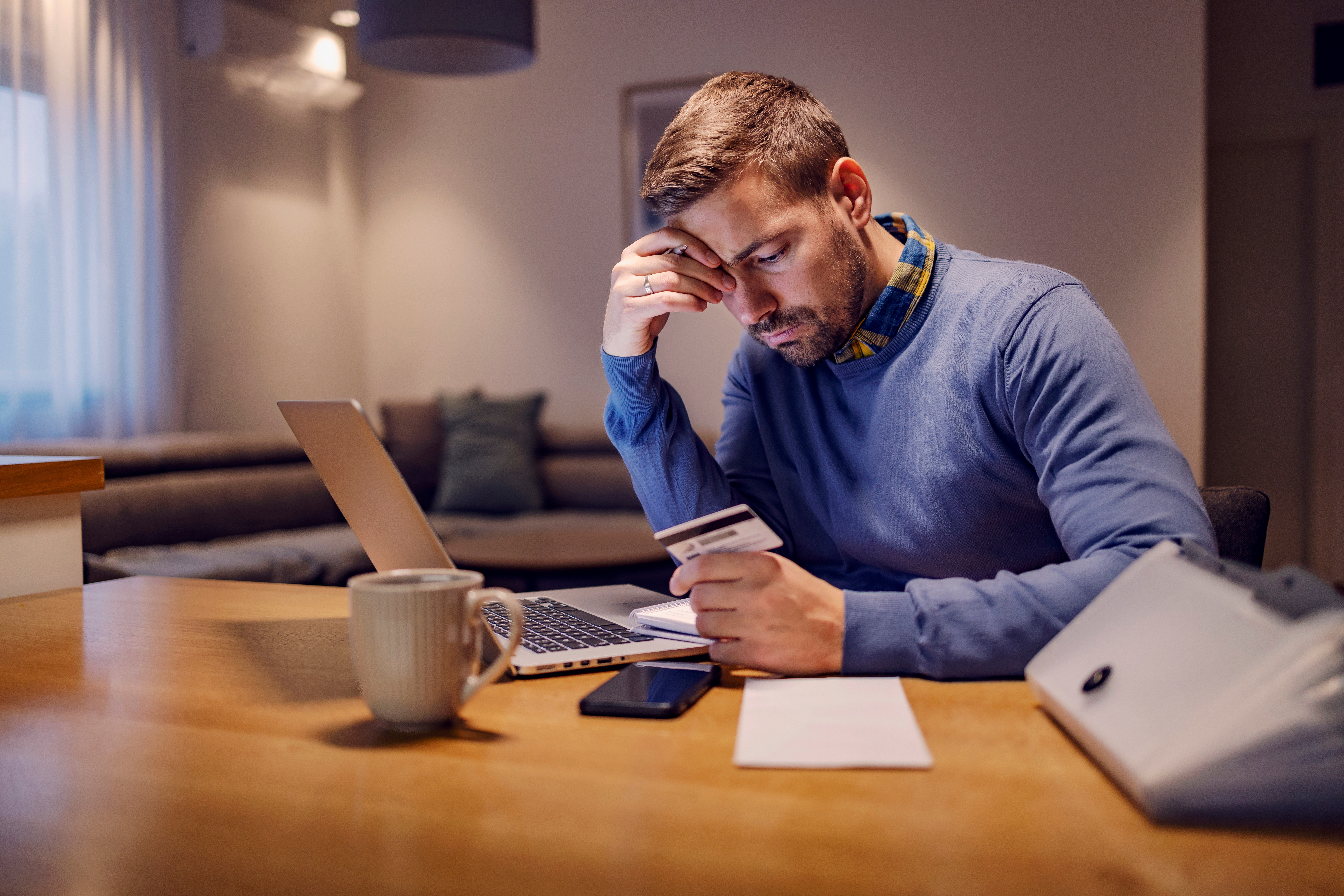 A worried man looking at his credit card with no invoice and having troubles with payment while sitting at home.