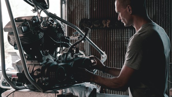 A mechanic working on a motorcycle engine in a workshop.